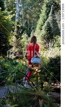 A girl on a walk, shot from behind. She's walking along a path in the arboretum, examining the plants A girl on a walk, shot from behind. She's walking along a path in the arboretum, examining the plants 139719906