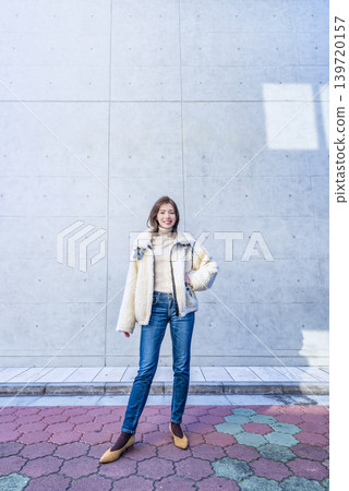 A young woman in casual attire standing in front of a concrete wall. A young woman in casual attire standing in front of a concrete wall. 139720157