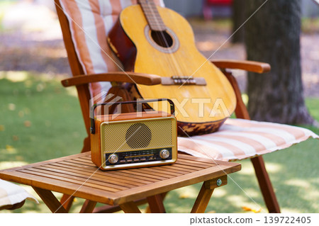 Outdoor garden relaxation area with wooden chair acoustic guitar and vintage radio leisure scene Outdoor garden relaxation area with wooden chair acoustic guitar and vintage radio leisure scene 139722405