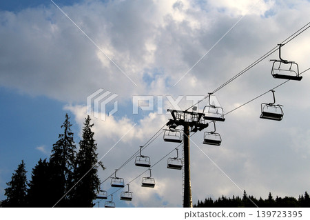 Silhouette of a chairlift over a forest on a mountain slope 139723395