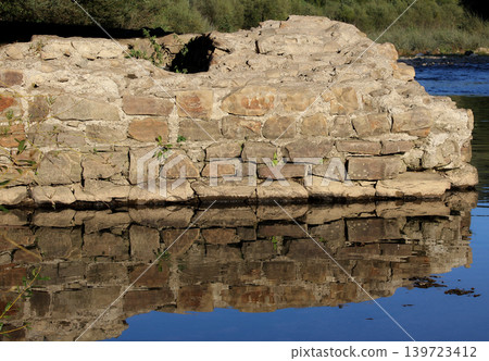 The remains of a brick bridge destroyed by time are reflected in the river water The remains of a brick bridge destroyed by time are reflected in the river water 139723412