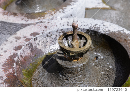 Ornate brass drinking fountain nozzle rises from a weathered stone basin Ornate brass drinking fountain nozzle rises from a weathered stone basin 139723640