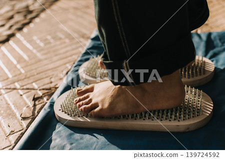 Feet standing on a Sadhu board (Yoga board) with sharp nails outdoor. Practice yoga, meditation, concentration. Feet standing on a Sadhu board (Yoga board) with sharp nails outdoor. Practice yoga, meditation, concentration. 139724592
