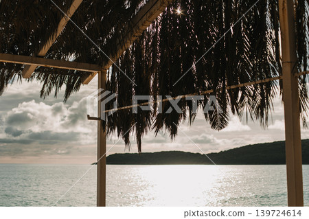 Gazebo made of palm leaves on the seashore at sunset. 139724614