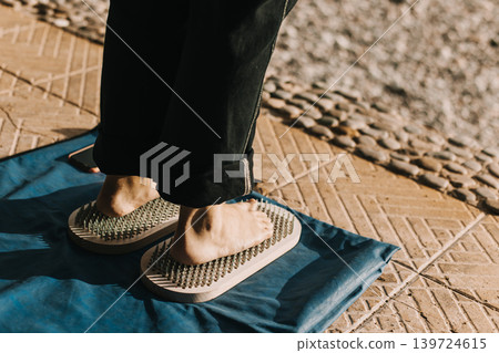 Feet standing on a Sadhu board (Yoga board) with sharp nails outdoor. Feet standing on a Sadhu board (Yoga board) with sharp nails outdoor. 139724615