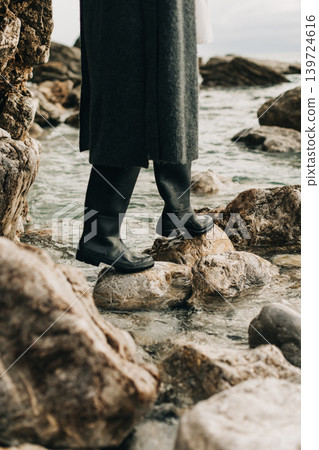 Girl in rubber boots on the rocks by the sea. 139724616