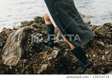 Girl in rubber boots on the rocks by the sea. Girl in rubber boots on the rocks by the sea. 139724718