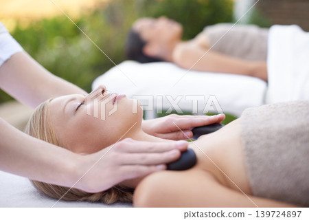 Young woman, hands and hot stone massage in spa, outdoor and wellness on bed for physical therapy. People, heat or masseuse for body treatment for detox, pain or muscle comfort with health at resort Young woman, hands and hot stone massage in spa, outdoor and wellness on bed for physical therapy. People, heat or masseuse for body treatment for detox, pain or muscle comfort with health at resort 139724897