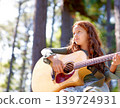Nature, camp and girl kid with guitar for entertainment, talent or music in woods or forest. Playing, musician and child with acoustic string instrument outdoor in park or field on weekend trip. 139724931
