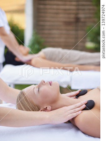 Women, health and massage with hot stones, wellness and peace with hands for shoulder at spa. People, comfort and zen for physical therapy by masseuse, body treatment and detox on bed at resort 139724974