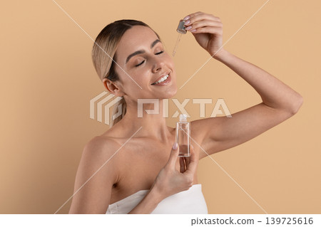 Happy young woman holding serum dropper up and smiling with eyes closed Happy young woman holding serum dropper up and smiling with eyes closed 139725616