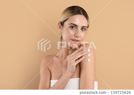 Young woman applying cream dots on her shoulder and looks at camera 139725626