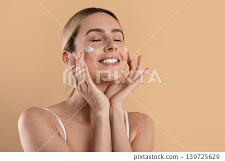 Happy young woman applying moisturizing face cream for healthy glowing skin Happy young woman applying moisturizing face cream for healthy glowing skin 139725629