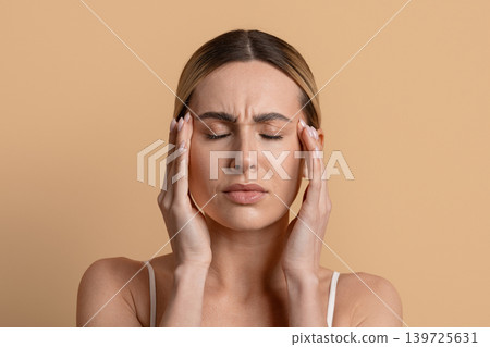 Young woman with closed eyes presses hands to temples with pained expression Young woman with closed eyes presses hands to temples with pained expression 139725631
