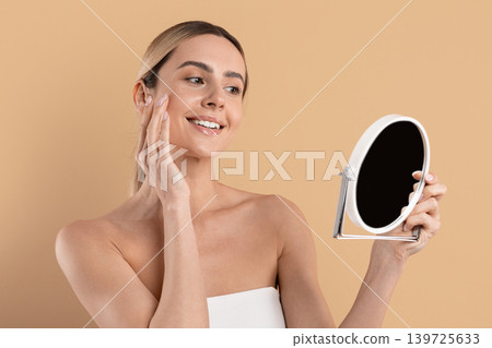 Smiling young woman looking into handheld mirror and touching her cheek 139725633