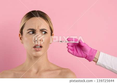 Nervous young woman reacting to cosmetic injection syringe near her face Nervous young woman reacting to cosmetic injection syringe near her face 139725644