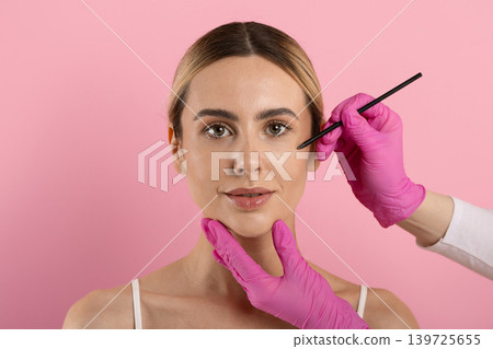 Doctor marking face of young woman with pencil before cosmetic procedure Doctor marking face of young woman with pencil before cosmetic procedure 139725655