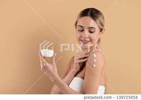 Beautiful young woman applying moisturizing body cream on shoulder on beige background Beautiful young woman applying moisturizing body cream on shoulder on beige background 139725658