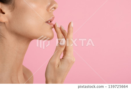 Closeup side view of young woman touching glossy lips on pink background Closeup side view of young woman touching glossy lips on pink background 139725664