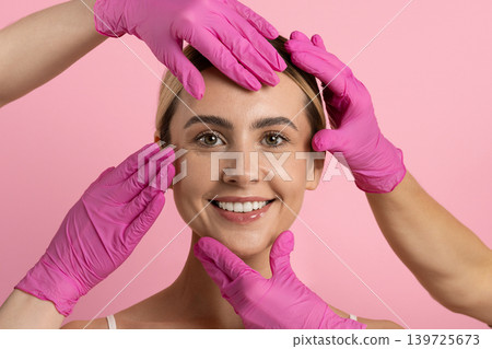 Smiling woman with glowing skin surrounded by multiple pink-gloved hands touching face Smiling woman with glowing skin surrounded by multiple pink-gloved hands touching face 139725673