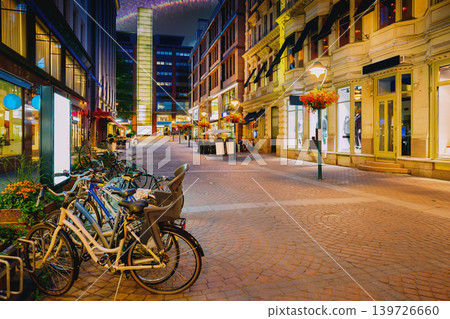 Helsinki, Finland. Bicycles Parked Near Storefronts In Kluuvikatu Street. Night Street In Kluuvi District In Evening Or Night Illumination. Quiet Pedestrian Street with Bicycles in Helsinki Helsinki, Finland. Bicycles Parked Near Storefronts In Kluuvikatu Street. Night Street In Kluuvi District In Evening Or Night Illumination. Quiet Pedestrian Street with Bicycles in Helsinki 139726660