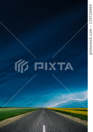 Open asphalt countryside road through fields with yellow flowering canola rapecolza in spring sunny day white clouds on blue sky storm bad weather thunder flash Open asphalt countryside road through fields with yellow flowering canola rapecolza in spring sunny day white clouds on blue sky storm bad weather thunder flash 139726664