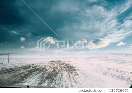 Snowdrift sweeping across a rural road under a bright winter sky Snowdrift sweeping across a rural road under a bright winter sky 139726671