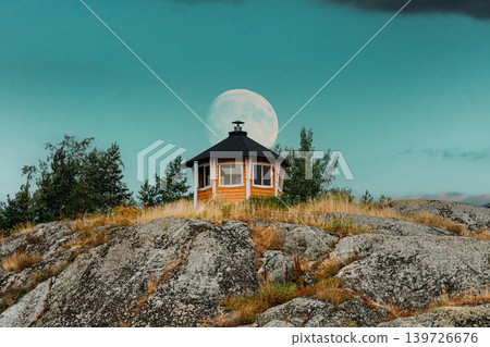 Small Finnish Wooden Cabin on a Rocky Hill with a Full Moon. Small Finnish Wooden Cabin on a Rocky Hill with a Full Moon. 139726676