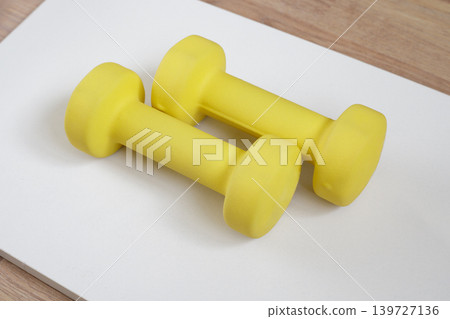 Small yellow dumbbells on a light gray mat. Sports equipment. Small yellow dumbbells on a light gray mat. Sports equipment. 139727136