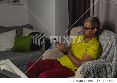 Man relaxing in armchair while browsing smartphone 139727398