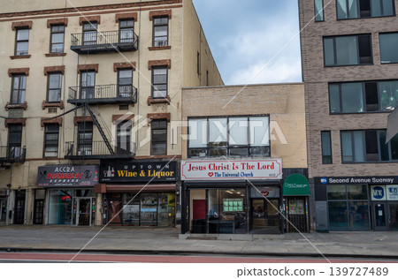 New york, usa august 18,2024. Harlem street showing diverse architecture, fire escapes, and storefronts like an african restaurant, liquor store, and church 139727489