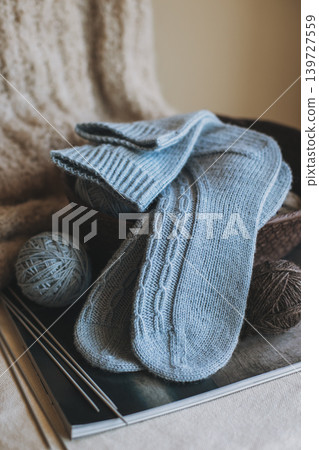 Hand knitted socks with needles and yarn ball in a basket. Concept for handmade and hygge slow life. Hand knitted socks with needles and yarn ball in a basket. Concept for handmade and hygge slow life. 139727559