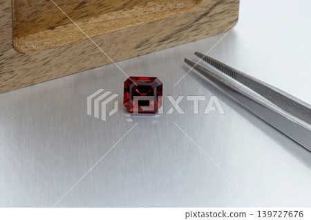 macro mineral faceted stone Garnet with tweezers on a gray background macro mineral faceted stone Garnet with tweezers on a gray background 139727676