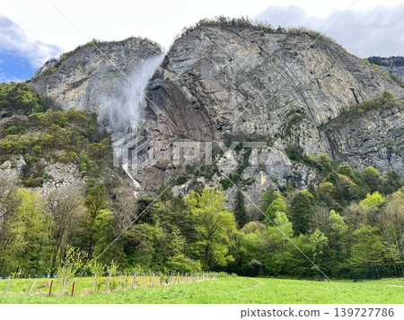 Majestic rocky mountain landscape with cascading waterfall surrounded by lush green trees 139727786