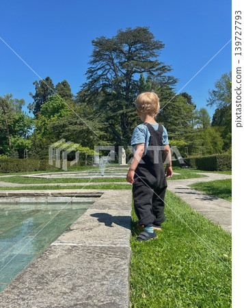 Young child with blonde hair wearing black overalls and blue shirt stands Young child with blonde hair wearing black overalls and blue shirt stands 139727793