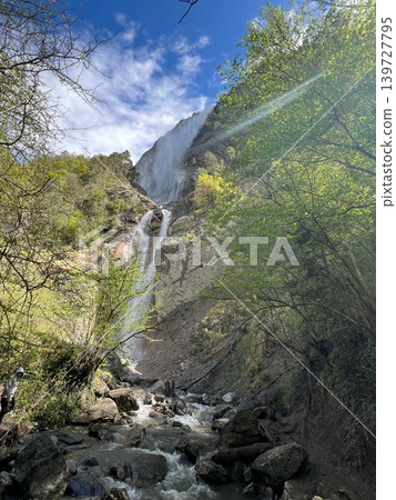 Waterfall cascading down rocky cliff surrounded by lush greenery and trees, with Waterfall cascading down rocky cliff surrounded by lush greenery and trees, with 139727795