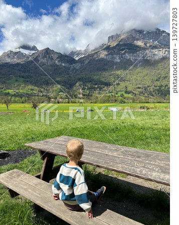 Young child with light brown hair sitting on wooden picnic table, gazing Young child with light brown hair sitting on wooden picnic table, gazing 139727803