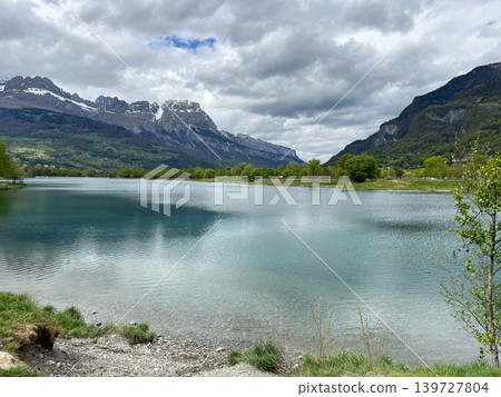 Scenic view of a tranquil lake surrounded by lush greenery and majestic Scenic view of a tranquil lake surrounded by lush greenery and majestic 139727804
