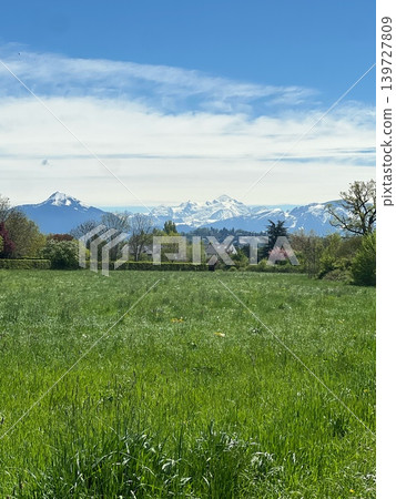Snow-capped mountains rise majestically above a lush green field under a Snow-capped mountains rise majestically above a lush green field under a 139727809