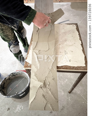A builder applies cement adhesive to a long porcelain tile. A builder applies cement adhesive to a long porcelain tile. 139728036