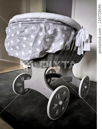 A retro wicker baby cradle on wheels in a room interior. A retro wicker baby cradle on wheels in a room interior. 139728040