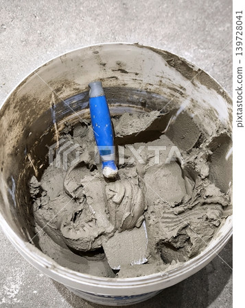Construction mortar or tile adhesive in a plastic bucket, with a trowel Construction mortar or tile adhesive in a plastic bucket, with a trowel 139728041