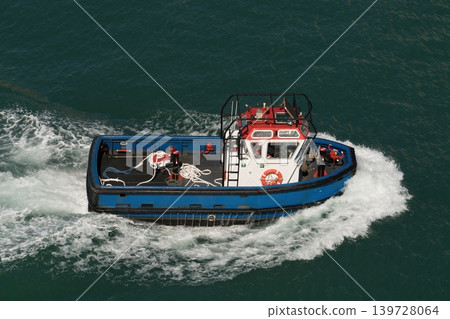 Blue harbor tugboat moving through green water with foamy wake 139728064