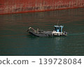 Small service workboat beside red ship hull in harbor water 139728084
