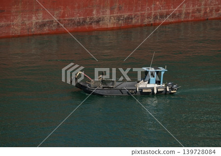 Small service workboat beside red ship hull in harbor water Small service workboat beside red ship hull in harbor water 139728084