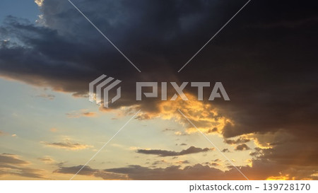 Dark dramatic grey storm clouds illuminated by bright golden sunlight in blue sky at sunset, dramatic atmosphere of weather change Dark dramatic grey storm clouds illuminated by bright golden sunlight in blue sky at sunset, dramatic atmosphere of weather change 139728170