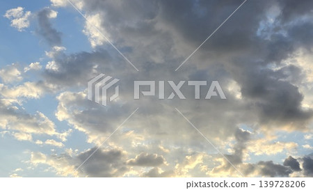 Blue sky with dramatic dark grey and fluffy white clouds illuminated by warm sunlight at sunset or sunrise, concept of weather changes and heaven Blue sky with dramatic dark grey and fluffy white clouds illuminated by warm sunlight at sunset or sunrise, concept of weather changes and heaven 139728206