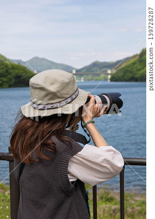 A woman photographs a lake in early summer at Lake Yamba-Agatsuma. A woman photographs a lake in early summer at Lake Yamba-Agatsuma. 139728287
