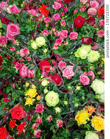 Bright colors of pink, red, and yellow rose bouquets fill the flower market. People walk by, choosing flowers for various occasions and events. The market is lively and vibrant. 139728300