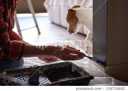 Person paints lower wall edge with small brush near tray on protective sheet Person paints lower wall edge with small brush near tray on protective sheet 139728682